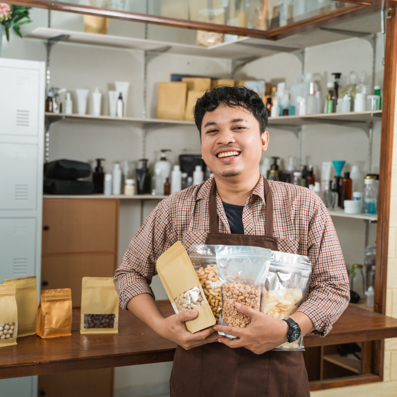 Emprendedor sonriente en su tienda de productos orgánicos, asesorado por Llamaalcontador.cl para gestión contable y fiscal de pequeñas empresas.